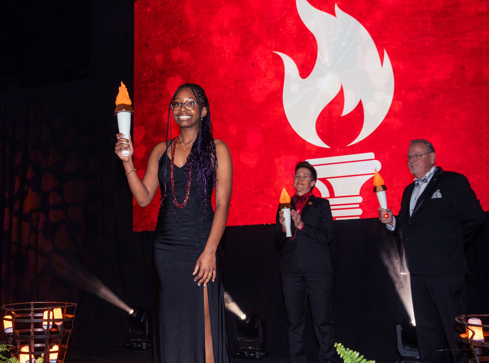 Three people holding up lit torches in front of heart and torch icon.